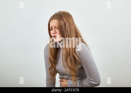 Schöne Frau im grauen Pullover im Hintergrund hat Schmerzen im Magen oder Magen Stockfoto