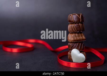 Stapel von Schokoladenbonbons und rotem Band auf schwarzem Hintergrund. Konzentrieren Sie sich auf Pralinen Stockfoto