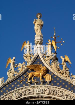 Statue von San Marcos über dem von Venedig geflügelten Löwen an der Fassade der Markusbasilika in Venedig Stockfoto