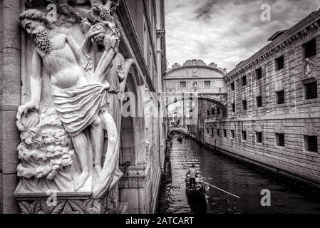 Venedig Stadtbild mit alter Skulptur in Schwarz-Weiß, Italien. Touristengondeln segeln unter der berühmten Brücke von Sighs. Es ist ein Wahrzeichen Venedigs. Romanti Stockfoto
