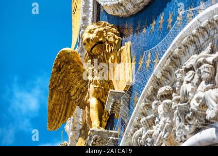 Der vergoldete Löwe auf der Spitze der Fassade der Markusbasilika (Markusdom) in Venedig, Italien. Der geflügelte Löwe ist ein Symbol Venedigs. Stockfoto