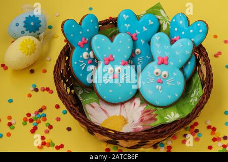 Ostern lustige blaue Kaninchen, hausgemalte Lebkuchen in Glasur in einem Korbkorb auf gelbem Hintergrund Stockfoto