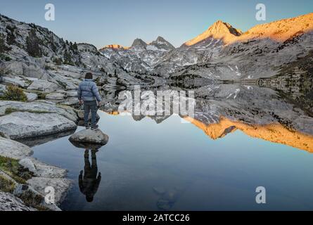 Mann, der auf einem Felsen steht und auf Mount Hooper Reflection in Rose Lake, Sierra National Forest, Kalifornien, USA blickt Stockfoto