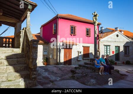 Combarro, Provinz Pontevedra, Galicien, Spanien: Lokale Frauen sitzen an einem kleinen Platz mit einer typischen Cruzeiro steinernen Kreuz in der traditionellen Altstadt von Stockfoto