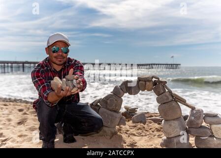 Juan Manuel Cisneros hielt am 30. Januar 2020 in Calif eine schwere Handvoll Felssteine am Fluss neben seinem neu errichteten Bogen am Strand von Ventura Stockfoto