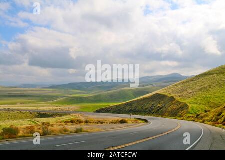 Strecke der geschwungenen einsamen Autobahn an einem wolkigen blauen Himmelstag Stockfoto