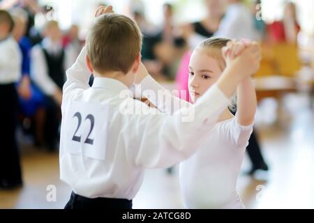 Fröhliche Kleinkinder nehmen am Tanzwettbewerb in der Tanzschule Teil. Junge und Mädchen, die in Weiß gekleidet sind, tanzten zusammen. Sport und Unterhaltung für Stockfoto