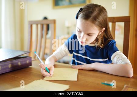 Schlaue kleine Schulmädchen machen ihre Hausaufgaben an ihrem Tisch zu Hause. Kinder lernen zu schreiben und zu lesen. Bildung und Lernen für Kinder. Stockfoto