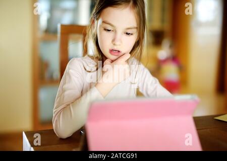 Schlaue kleine Schulmädchen machen ihre Hausaufgaben mit digitalem Tablet zu Hause. Untergeordnetes Element, das Gadgets zum Studium verwendet. Bildung und Lernen für Kinder. Stockfoto