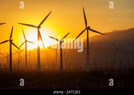 Der Himmel leuchtet orange über den Hügeln in Palm Springs mit Windmühlen im Vordergrund Stockfoto