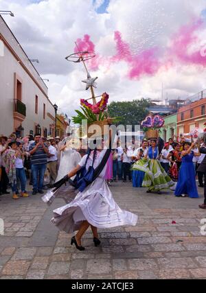 Frau dreht sich in fließendem traditionellem Outfit mit Blumenkorb, beleuchtet Einen Teil Der Traditionellen Hochzeitsparade (Calenda de Bodas) auf den Straßen von Oaxaca. Stockfoto