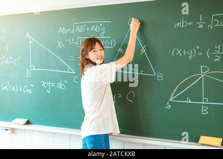 Studentin im Klassenzimmer, die auf mathematischen Gleichungen im Schwarzen Brett schreibt Stockfoto