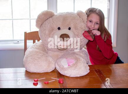 Süßes Mädchen teilt Valentinstag Leckereien mit einem Riesenbären Stockfoto