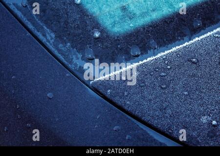 Nahaufnahme der T-Ecke der Haube eines Autos, bedeckt mit kondensiertem Eis auf Metall- und Glasflächen. Stockfoto