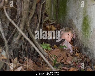 Eine alte, verlassene Puppe unter Blättern und Reben, in einer Gasse, im Stadtzentrum von Mobile, Alabama Stockfoto