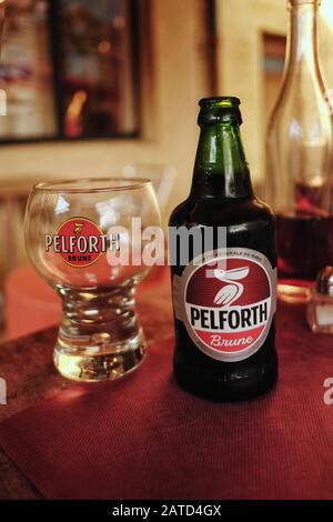 Eine Flasche PELFORTH Brune dunkles Bier mit einem passenden runden Markenglas für das nordfranzösische Bier, das am Nachmittag auf einem Café-Tisch fotografiert wurde Stockfoto