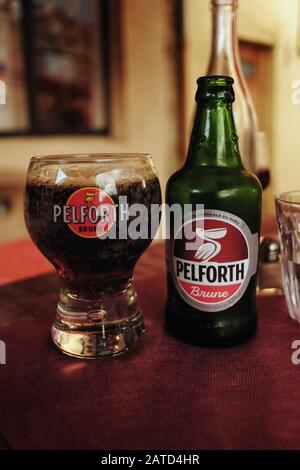 Eine Flasche PELFORTH Brune dunkles Bier mit einem passenden runden Markenglas für das nordfranzösische Bier, das am Nachmittag auf einem Café-Tisch fotografiert wurde Stockfoto