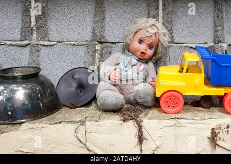 Eine Puppe und ein Plastikspielzeug-Lastwagen an der Zinnenblockwand, hinter einem Sparladen, in Springfield, Georgia. Stockfoto