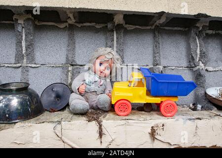 Eine Puppe und ein Plastikspielzeug-Lastwagen an der Zinnenblockwand, hinter einem Sparladen, in Springfield, Georgia. Stockfoto