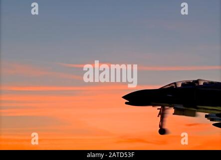 Silhouette eines historischen Kampfflugzeugs McDonnell Douglas F-4 Phantom II, der gegen die roten Wolken des Morgenhimmels über der Mobile Bay, Alabama, startete. Stockfoto