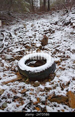 Ein alter, schneebedeckter Reifen auf der Seite eines Hügels an einem illegalen Müllhaldeplatz aus den 1950er und 1960er Jahren, südöstlich von Troy, Montana. Stockfoto