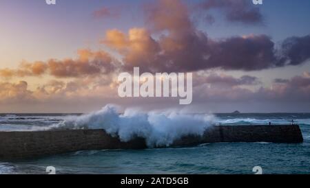 Wellen stürzen auf den Kai in Sennen Cove, Cornwall Stockfoto