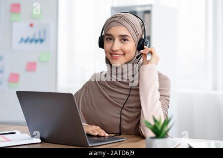 Schöne arabische Frau im Hijab, die ein Headset trägt, das in modernen Büros arbeitet Stockfoto