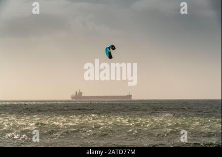 Ein Kiteboarder oder Paraborder segelt an der küste von cornwall mit einem Tankschiff dahinter, Großbritannien Stockfoto