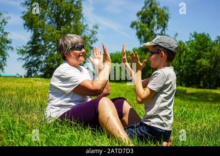 Ein Junge und eine Großmutter sitzen auf dem Rasen und spielen ein Spiel von Ladushki. Stockfoto