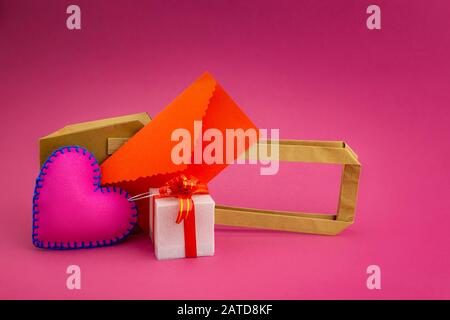 Liebe und romantische Botschaft Stillleben mit violett glühendem Herz, Kerze, dekorativen Geschenken und rotem Umschlag auf pinkfarbenem Hintergrund mit Kopierraum Stockfoto