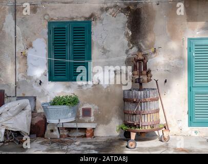 Alte, alte Weinpresse aus Holz, rustikal, in der Straßenszene des Dorfes mit anderen Gegenständen. Bolgheri, in der Toskana, Italien. Ländliches Leben. Stockfoto