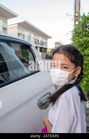 Ein kleines asiatisches Mädchen in einer Uniform, das beim Schulbesuch Masken trägt, um Keime zu verhindern Stockfoto