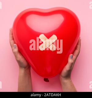 Frau, die Gebrochenes Herz mit Binde auf Rosa hält Stockfoto