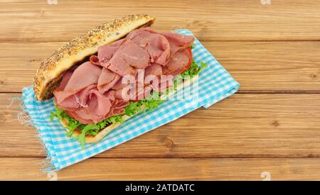 Würziges pastrami-fleisch und Salat-Sandwich in einer mit Saatgut bedeckten Brötchen, isoliert auf einem Holzhintergrund Stockfoto