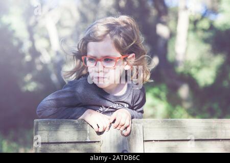 Porträt eines Jungen, der Brille trägt, die sich an einen Zaun lehnt, Spanien Stockfoto