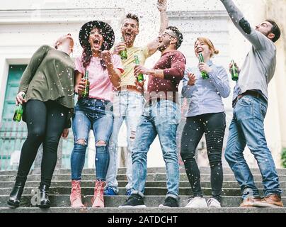 Fröhliche verrückte Freunde feiern auf der Straße Bier trinken und Konfetti werfen - Junge Studenten haben Spaß zusammen - Freundschafts- und Jugendkonzept Stockfoto