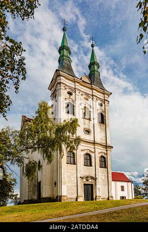 Krahulci/Tschechien - 27. September 2019: Blick auf eine Johannes von Nepomuk Kirche, ein weißes hohes Gebäude aus dem 18. Jahrhundert, das auf einem grünen Hügel steht. Stockfoto