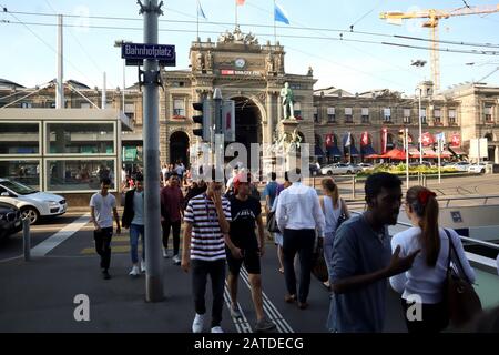 Zürich, Schweiz, 19. Juli 2019: Hauptbahnhof Zürich, altes Gebäude mit Fahnen und Drähten über der Straße, mit vorbeifahrenden Leuten Stockfoto