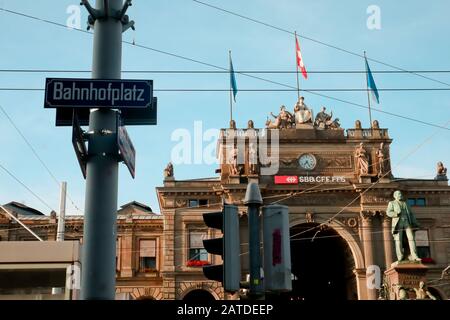 Zürich, Schweiz, 19. Juli 2019: Zürich Hauptbahnhof, altes Gebäude mit Fahnen und Leitungen oberhalb der Strasse, mit historischen Denkmal vor, Stockfoto