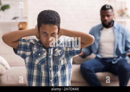 Teenager schwarzer Junge, der die Ohren schließt, um die Schelte des Vaters nicht zu hören Stockfoto