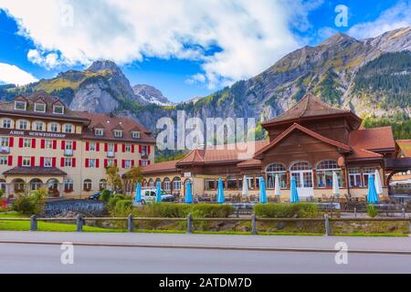 Kandersteg, Schweiz - 17. Oktober 2019: Straßenblick mit bunten Häusern im schweizer Dorf, Außenrestaurant und Bergpanorama Stockfoto