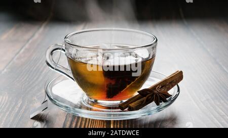 Transparente Tasse auf einer Untertasse mit Teebeutel, Zimtstäbchen und Anis auf dem Tisch Stockfoto