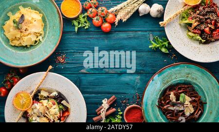 Ein Satz Geschirr. Pasta mit Parmesankäse und Gemüsesalat und Blaukäse. Draufsicht. Freier Speicherplatz für Ihren Text. Auf Holzgrund. Stockfoto