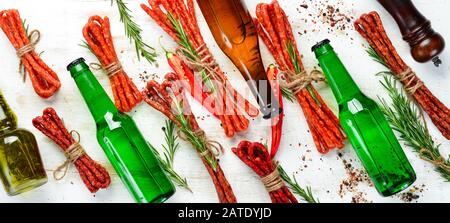 Bier in Flasche und geräucherte Wurst auf weißem Holzhintergrund. Bier, Kabanosy. Draufsicht. Freier Speicherplatz für Ihren Text. Stockfoto