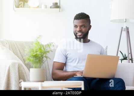 Positiver schwarzer Mann, der zu Hause auf einem Laptop tippt Stockfoto