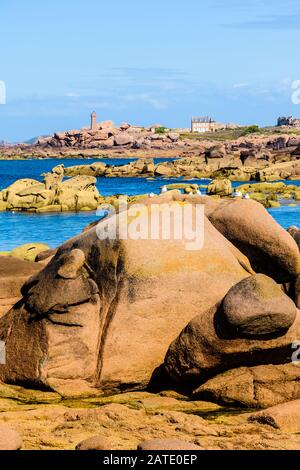 Seascape der Küste aus rosafarbenem Granit in der Bretagne, Frankreich, mit rosafarbenen Felsbrocken im Vordergrund und dem Leuchtturm Ploumanac'h in der Ferne. Stockfoto