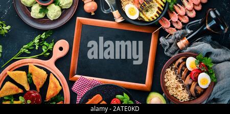 Asiatische Küche. Nudeln, Garnelen, Samsa, Khinkali. Auf schwarzem Holzhintergrund. Draufsicht. Freier Speicherplatz. Stockfoto
