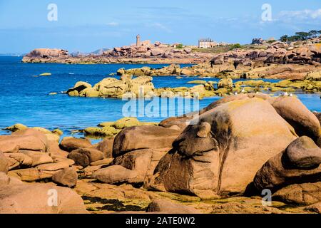 Seascape der Küste aus rosafarbenem Granit in der Bretagne, Frankreich, mit rosafarbenen Felsbrocken im Vordergrund und dem Leuchtturm Ploumanac'h in der Ferne. Stockfoto