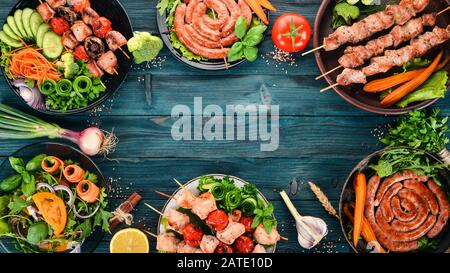 Eine Auswahl an Fleisch und frischem Gemüse. Grill, Würstchen, Steaks. Auf blauem Holzhintergrund. Kopierbereich. Stockfoto