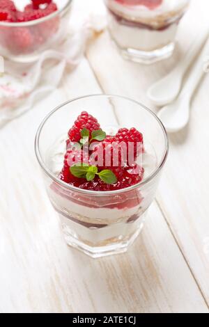 Käsekuchen mit Himbeeren in Brille auf weißem Holzhintergrund Stockfoto